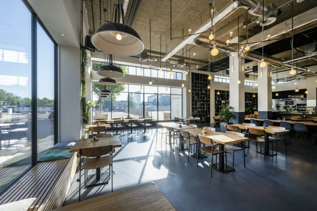 Moderne, ruim opgezette horecagelegenheid aan de Joan Muyskenweg met grote ramen, houten tafels en industriële verlichting.